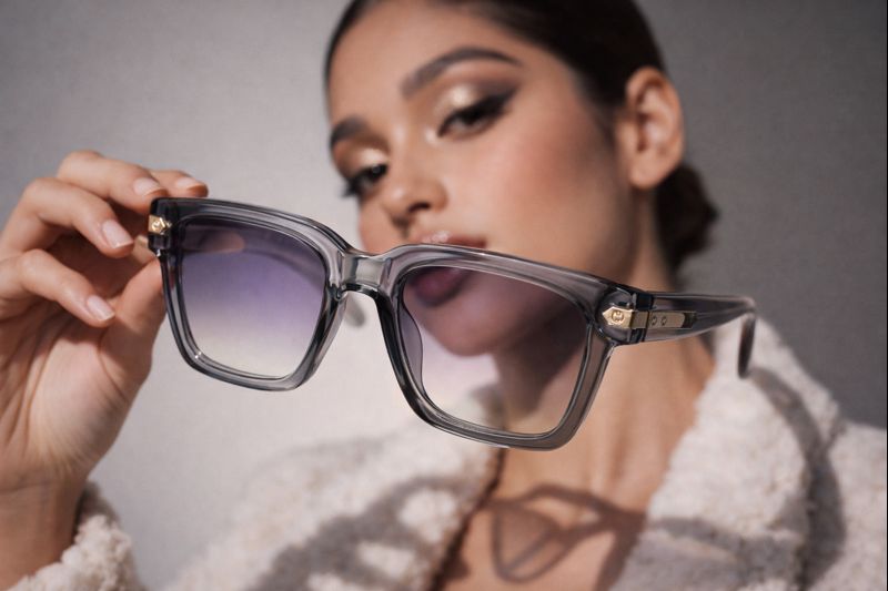 Frau hält eine graue quadratische Sonnenbrille mit transparenten Fassungen und Verlaufsgläsern für ein Porträt.