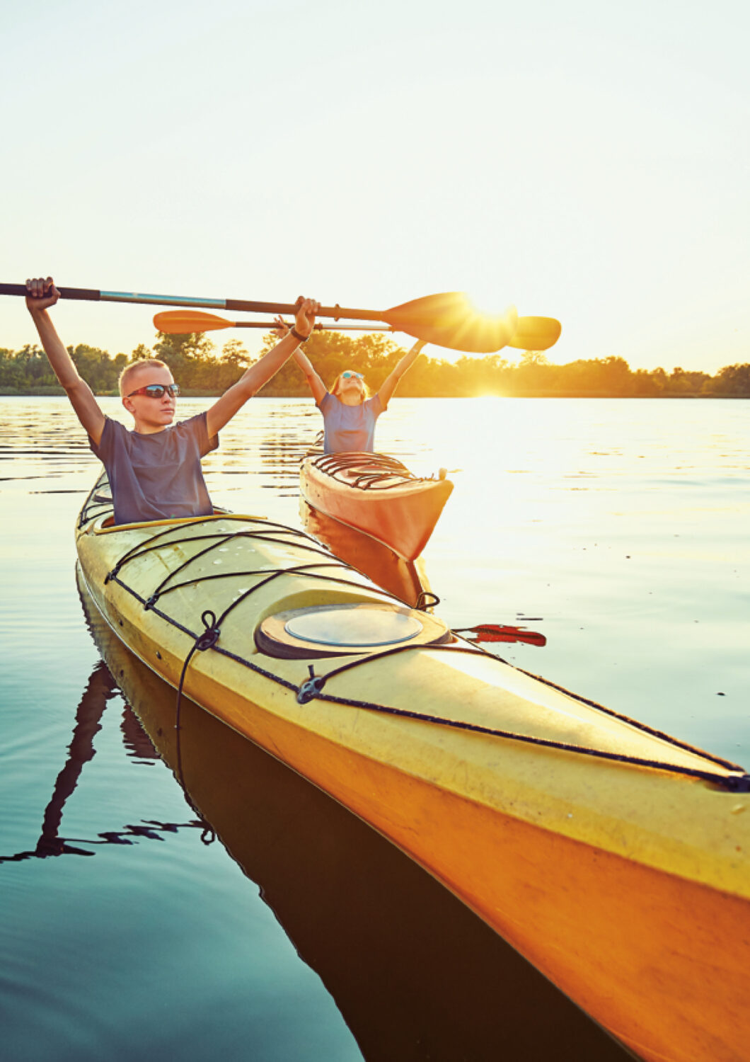 Deux personnes font du kayak sur un lac calme au coucher du soleil, le garçon devant portant des lunettes de sport.
