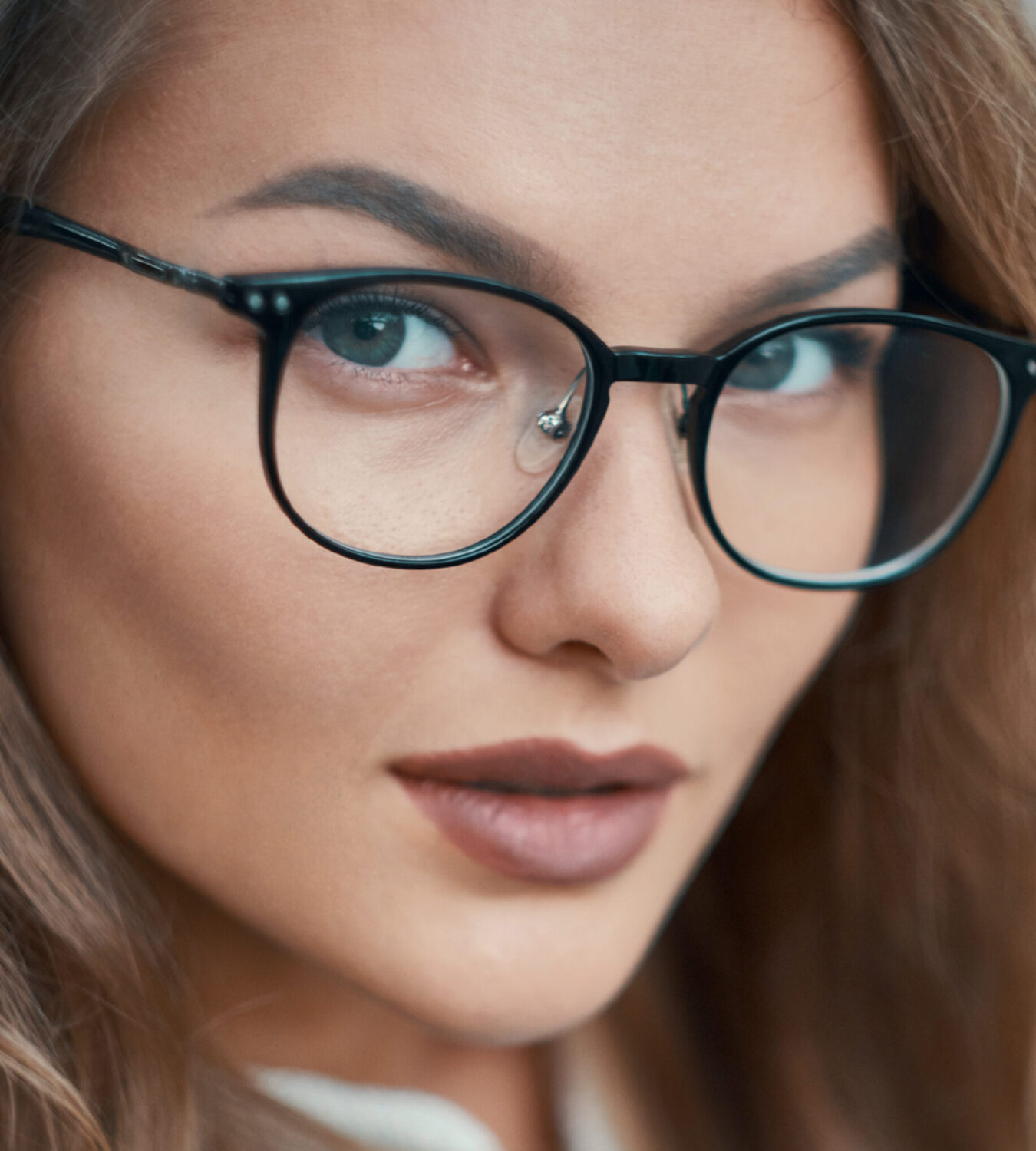 Gros plan sur une jeune femme aux cheveux ondulés et aux lunettes noires élégantes.