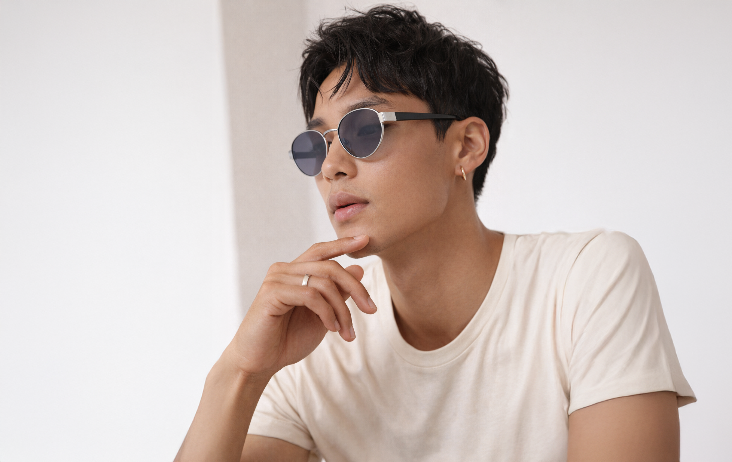 Homme élégant portant des lunettes de soleil rondes d'une collection d'optique, posant contre un mur blanc.