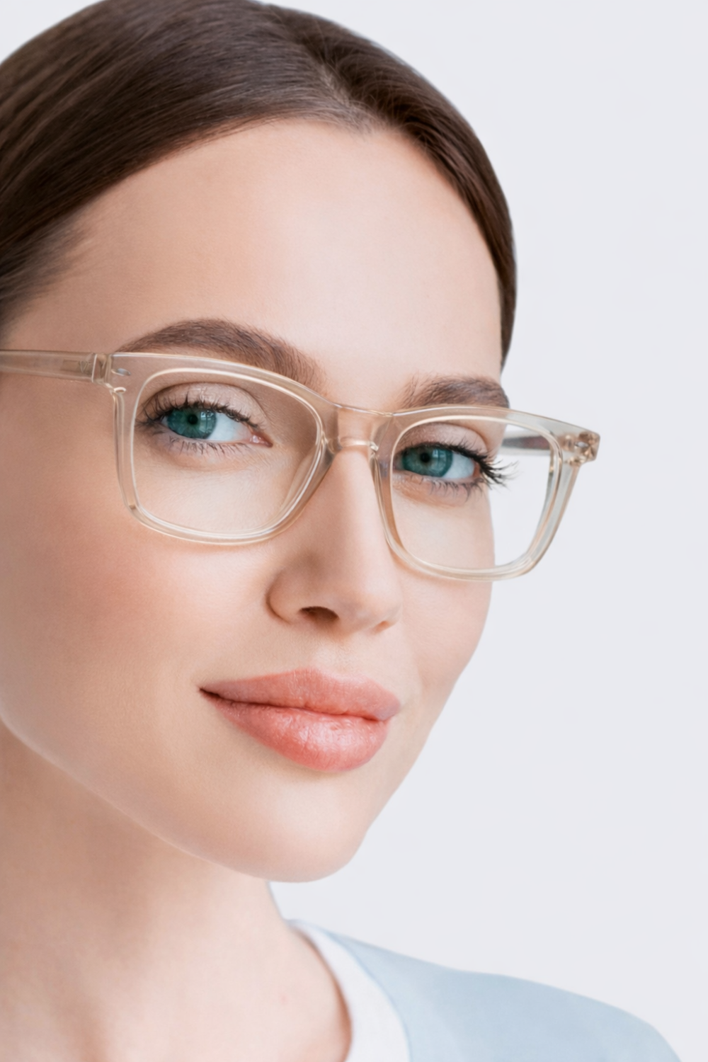 Mujer de pelo castaño lleva unas elegantes gafas transparentes de color azul claro sobre un fondo claro.