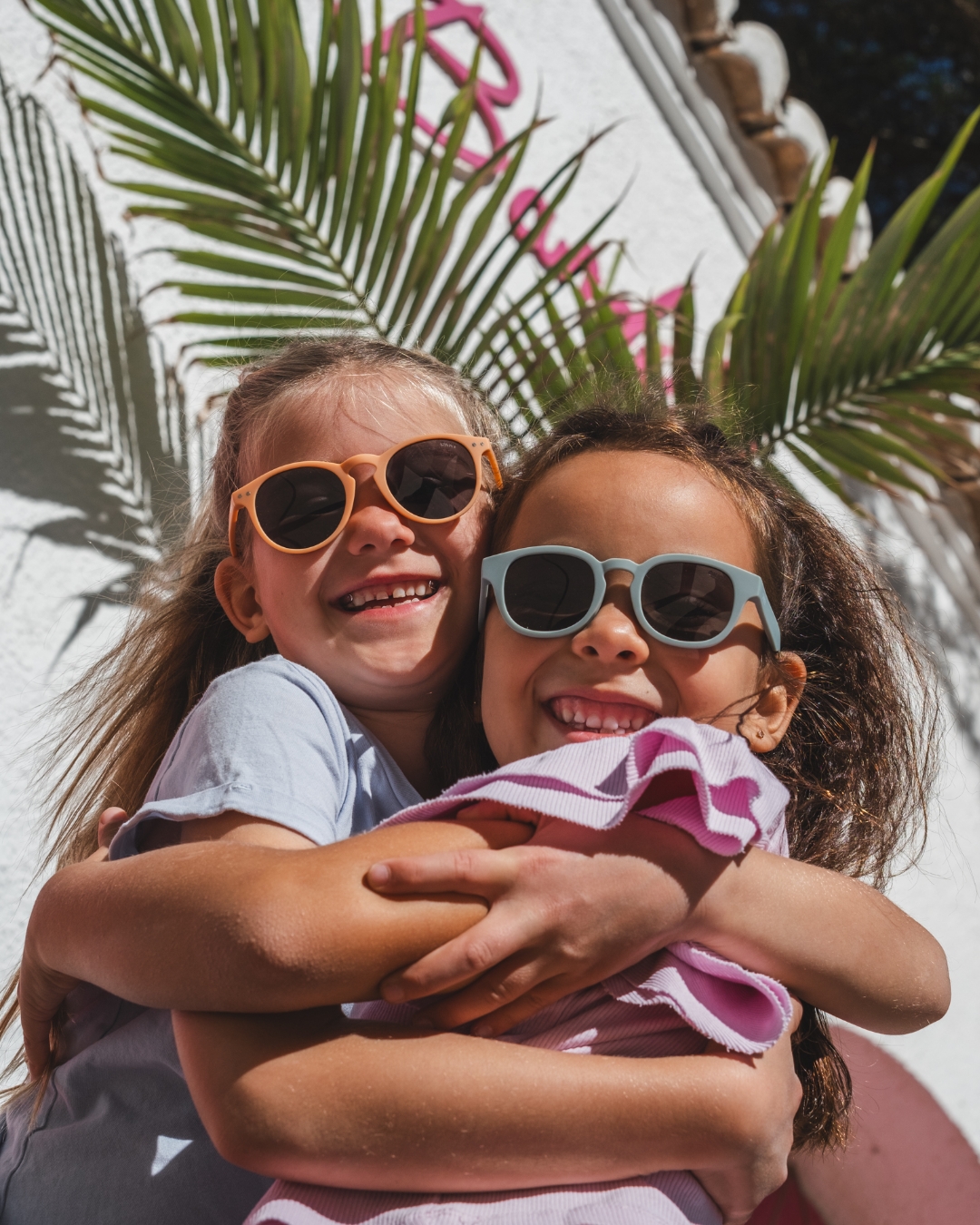 Dos chicas sonrientes abrazándose con gafas de sol a la moda de Okky.