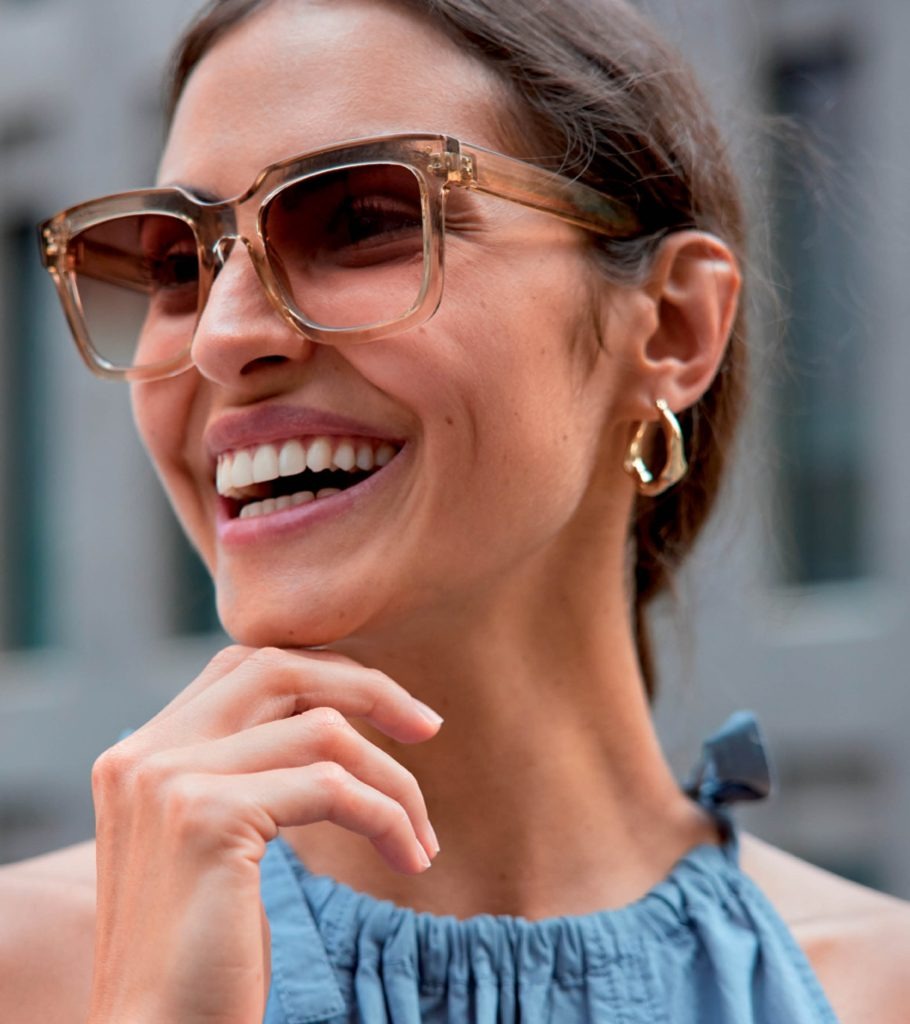 Mujer sonriente con elegantes gafas de sol cuadradas marrones y pendientes dorados.