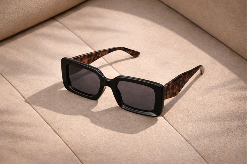 Stylish black rectangular sunglasses with panther-print legs on a soft beige background.