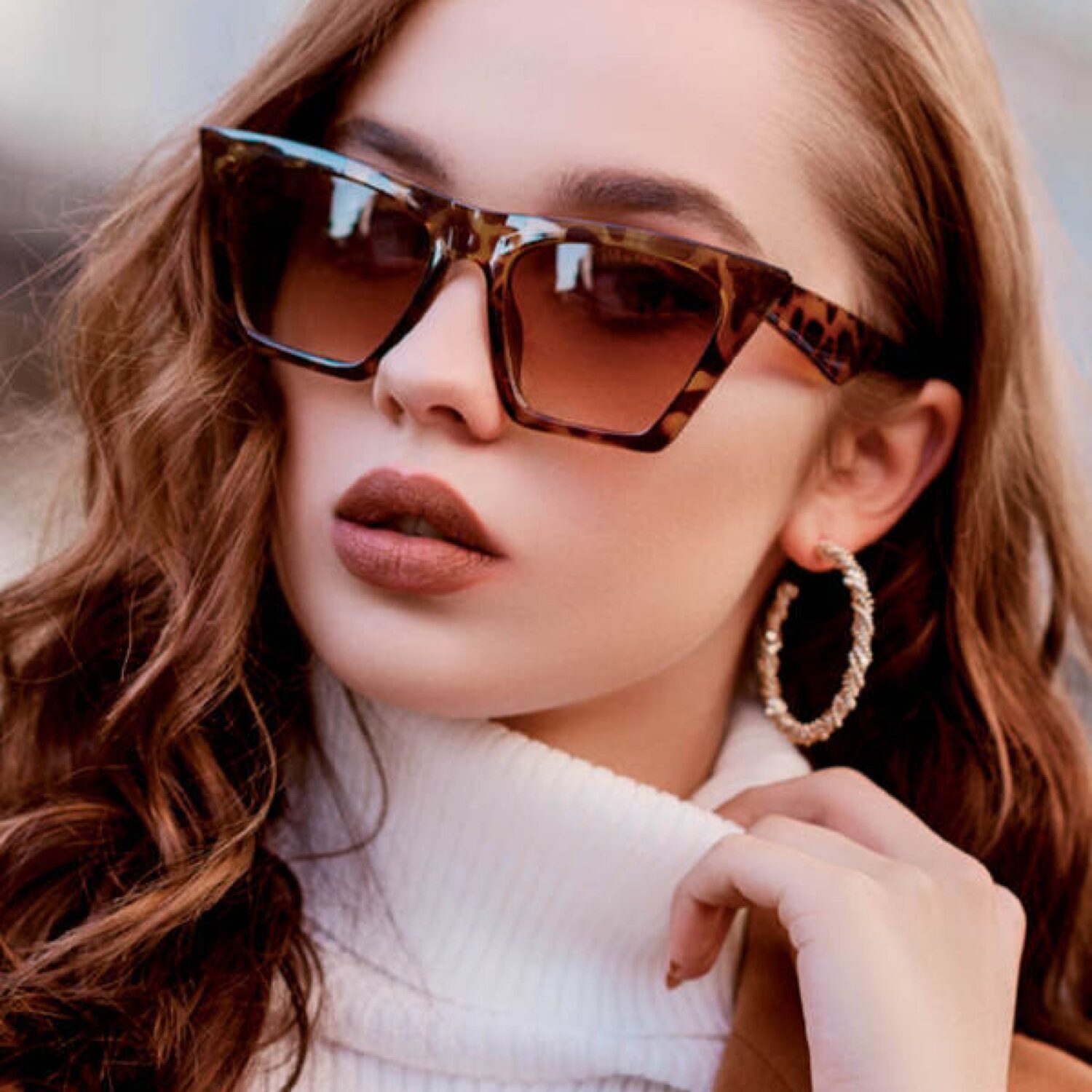 Woman wearing stylish panther-print sunglasses, a white turtleneck and large gold earrings.