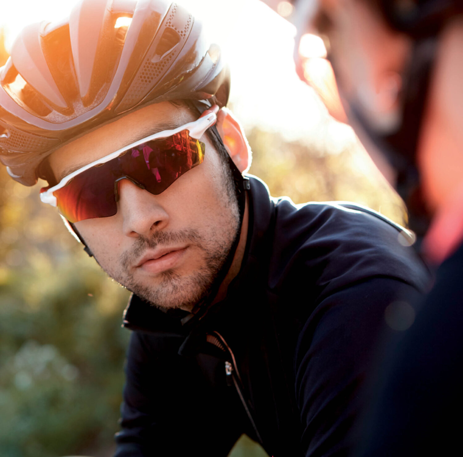 Cyclist wearing black helmet and white Revex sports sunglasses with red lenses in the outdoors.
