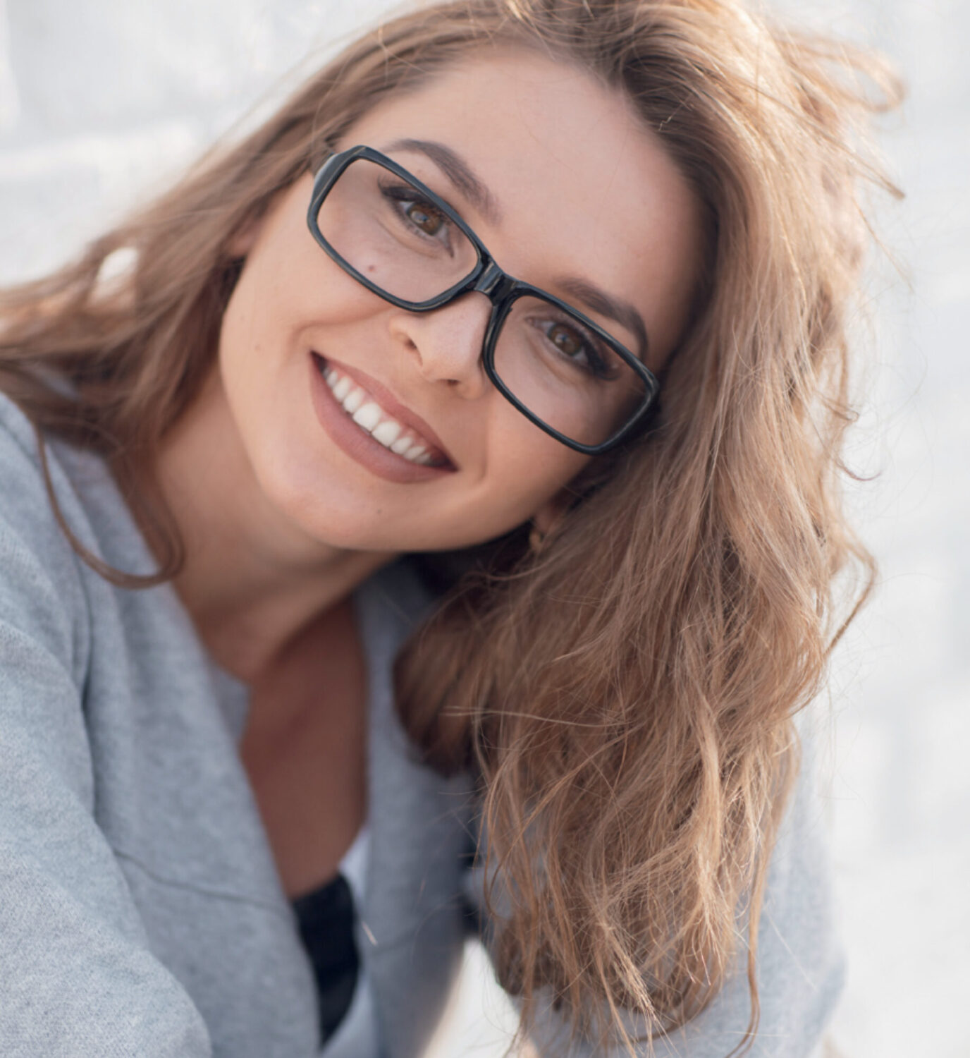 Portrait of a smiling young woman with fashionable black glasses and wavy brown hair.